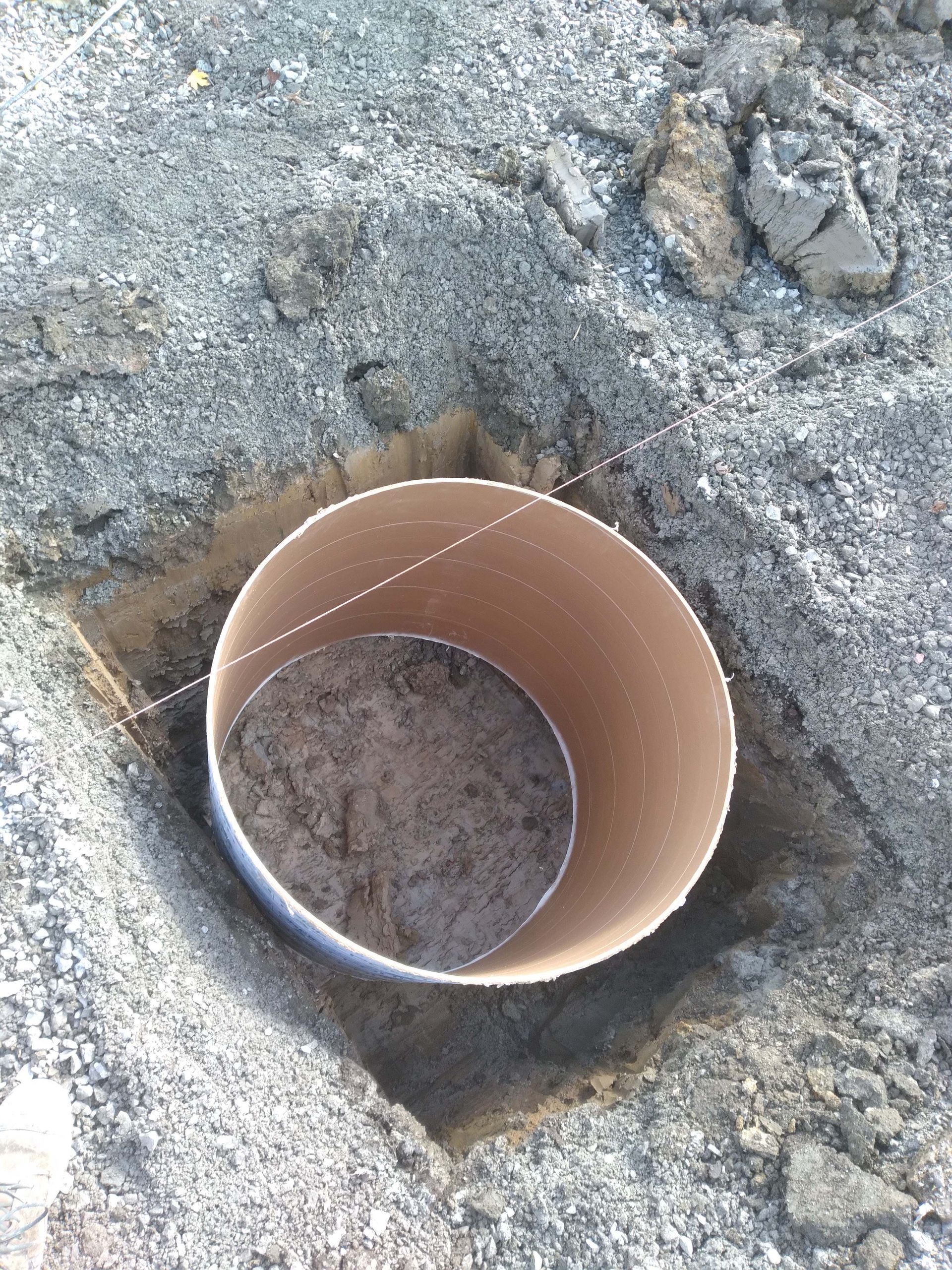 A cardboard tube in a square hole, with string across the top, in dirt, likely for a construction project.