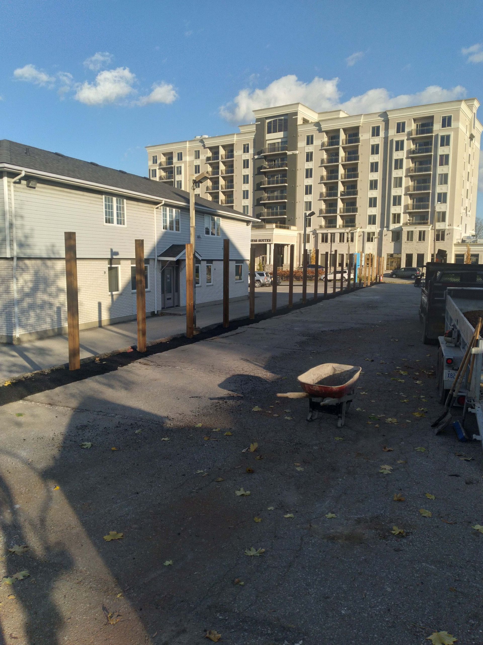 Gravel path with a newly built wooden fence. Large apartment building in the background on a sunny day.