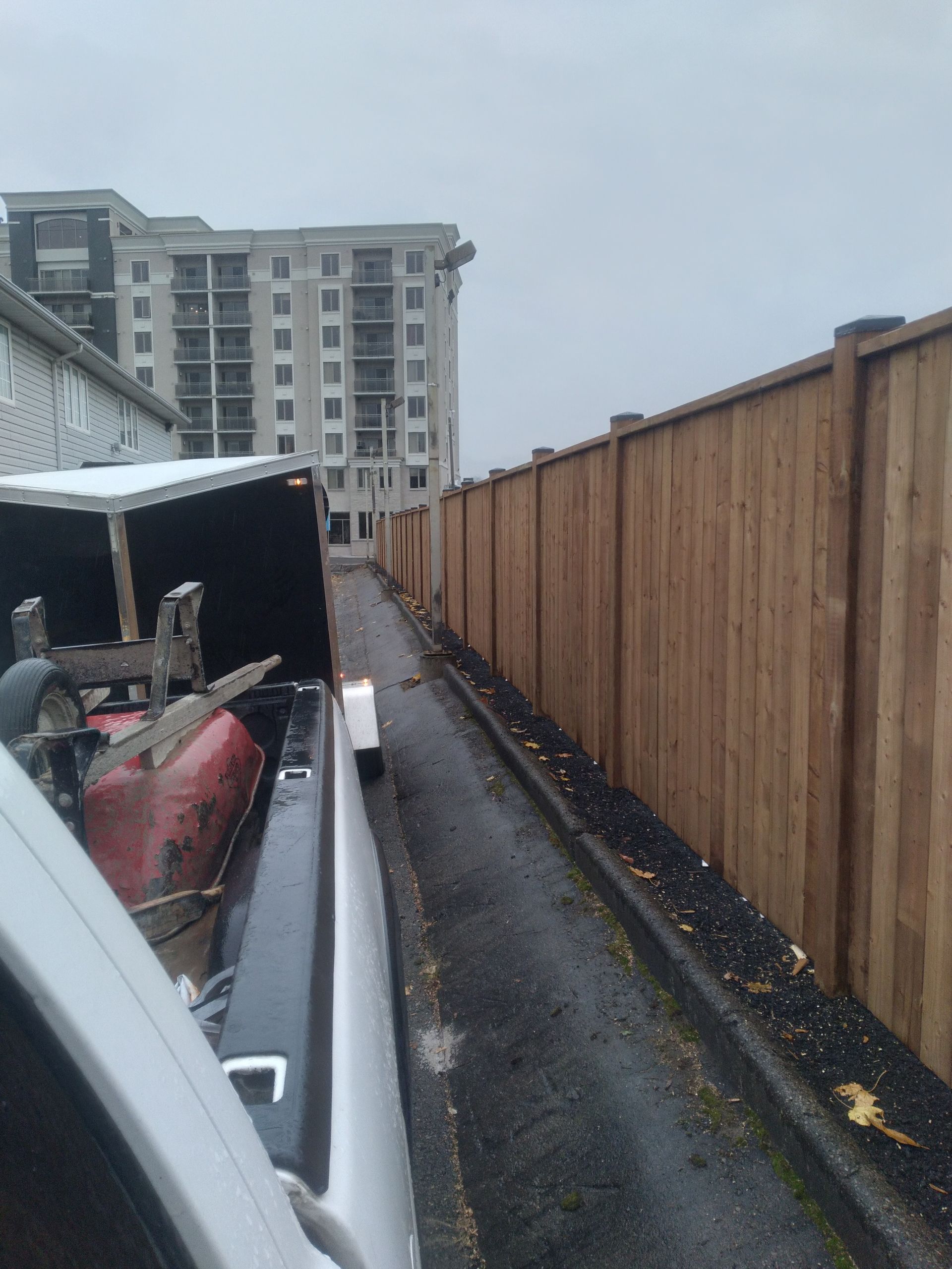 A truck bed loaded with equipment, driving down a narrow alley beside a wooden fence and a tall building.