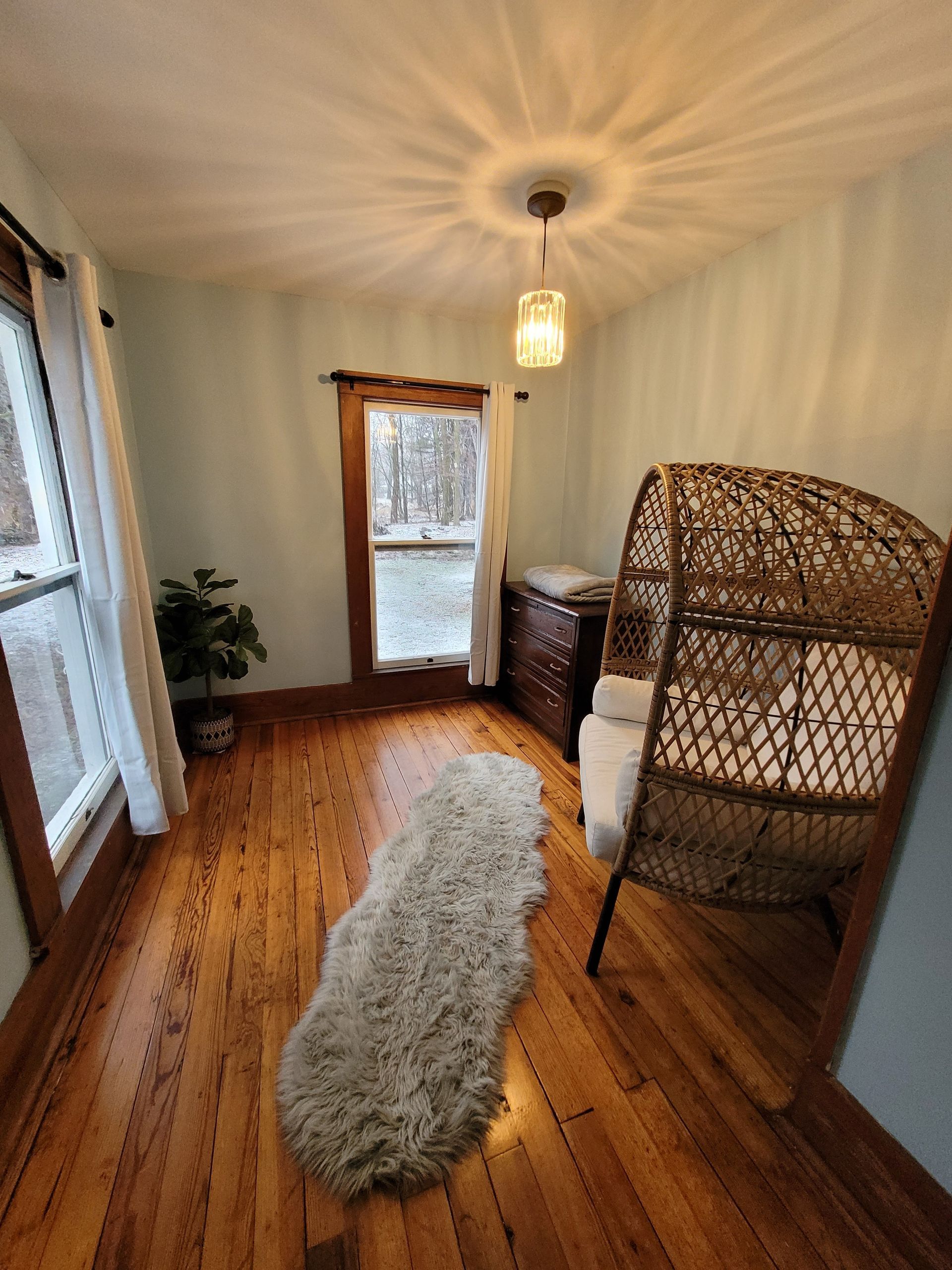 Cozy room with wooden floor, wicker chair, rug, and window overlooking snowy outdoors.