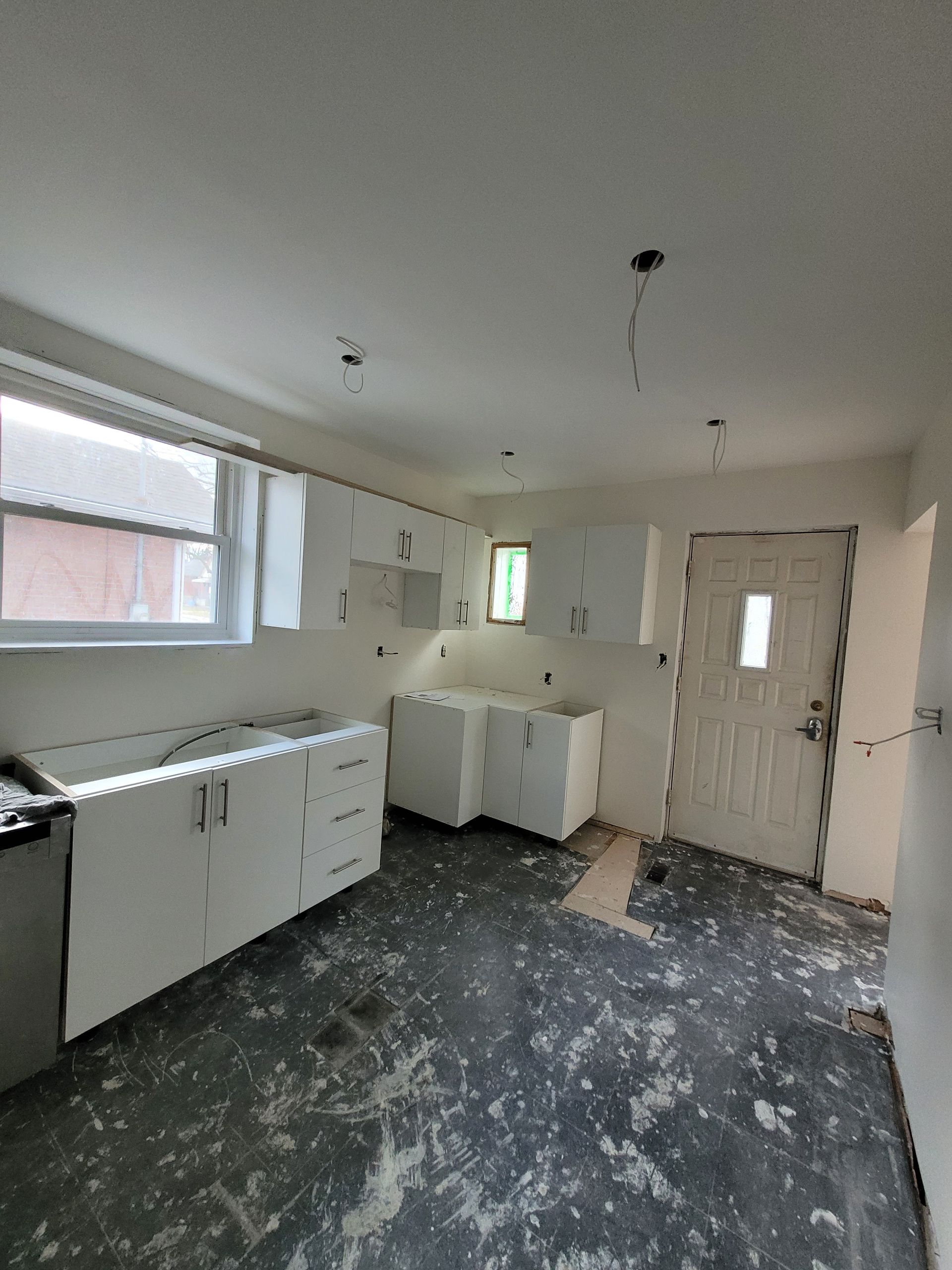 Kitchen renovation with white cabinets, bare walls, and dark floor.