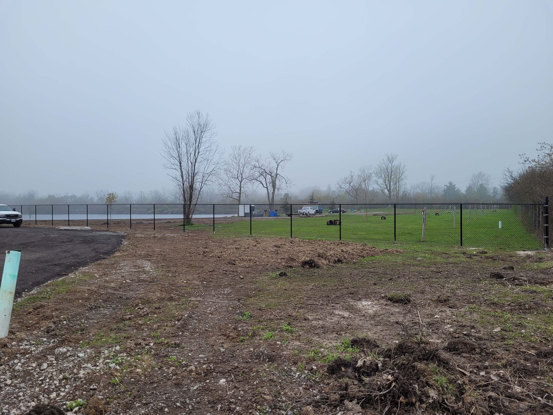 A chain-link fence in a field, on a gloomy day. A few trees are visible in the background.