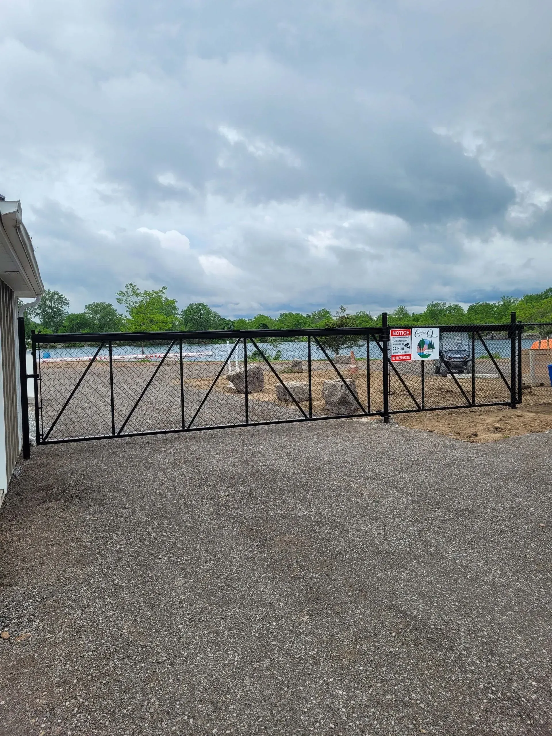 Black gate in front of a construction site, with gray gravel and cloudy sky.