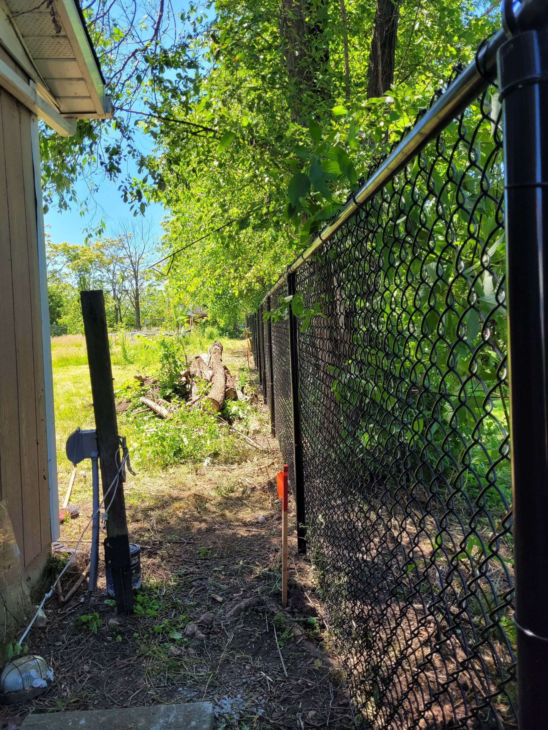 Black chain link fence along a narrow path, beside a building and greenery.