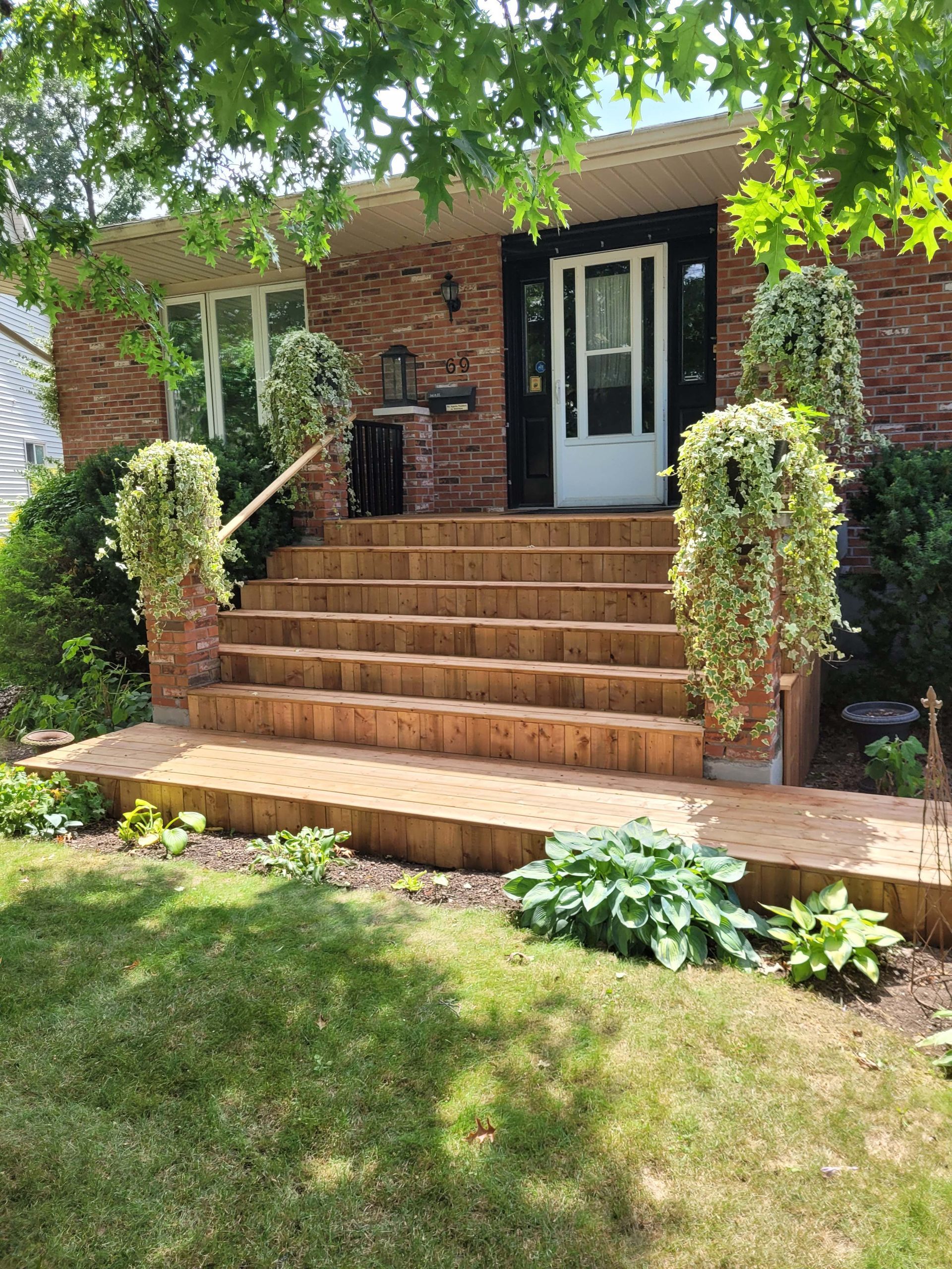 Brick house with wooden steps and hanging plants, on a sunny day.