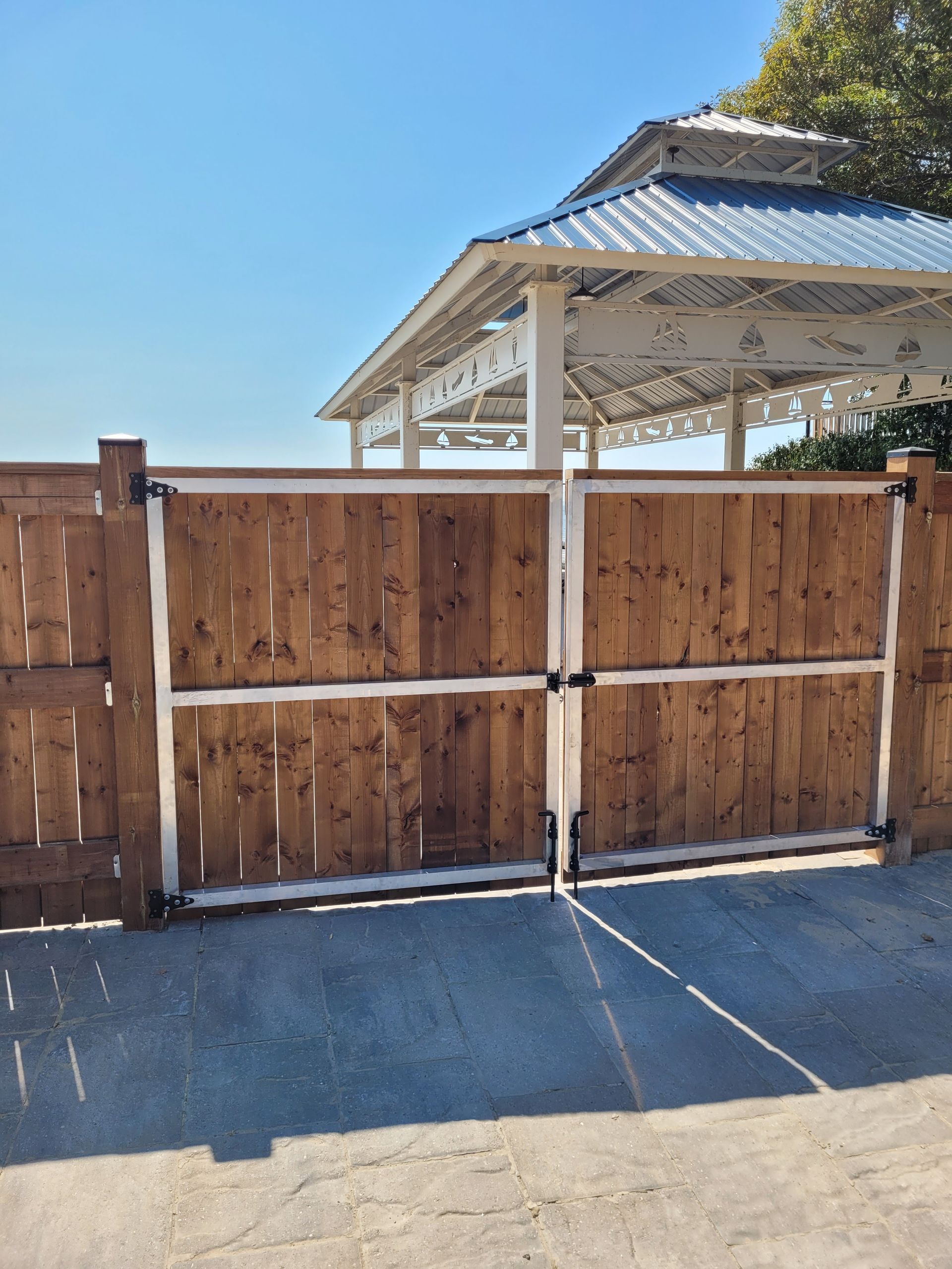 Wooden gate with metal frame in front of a gazebo on a sunny day.