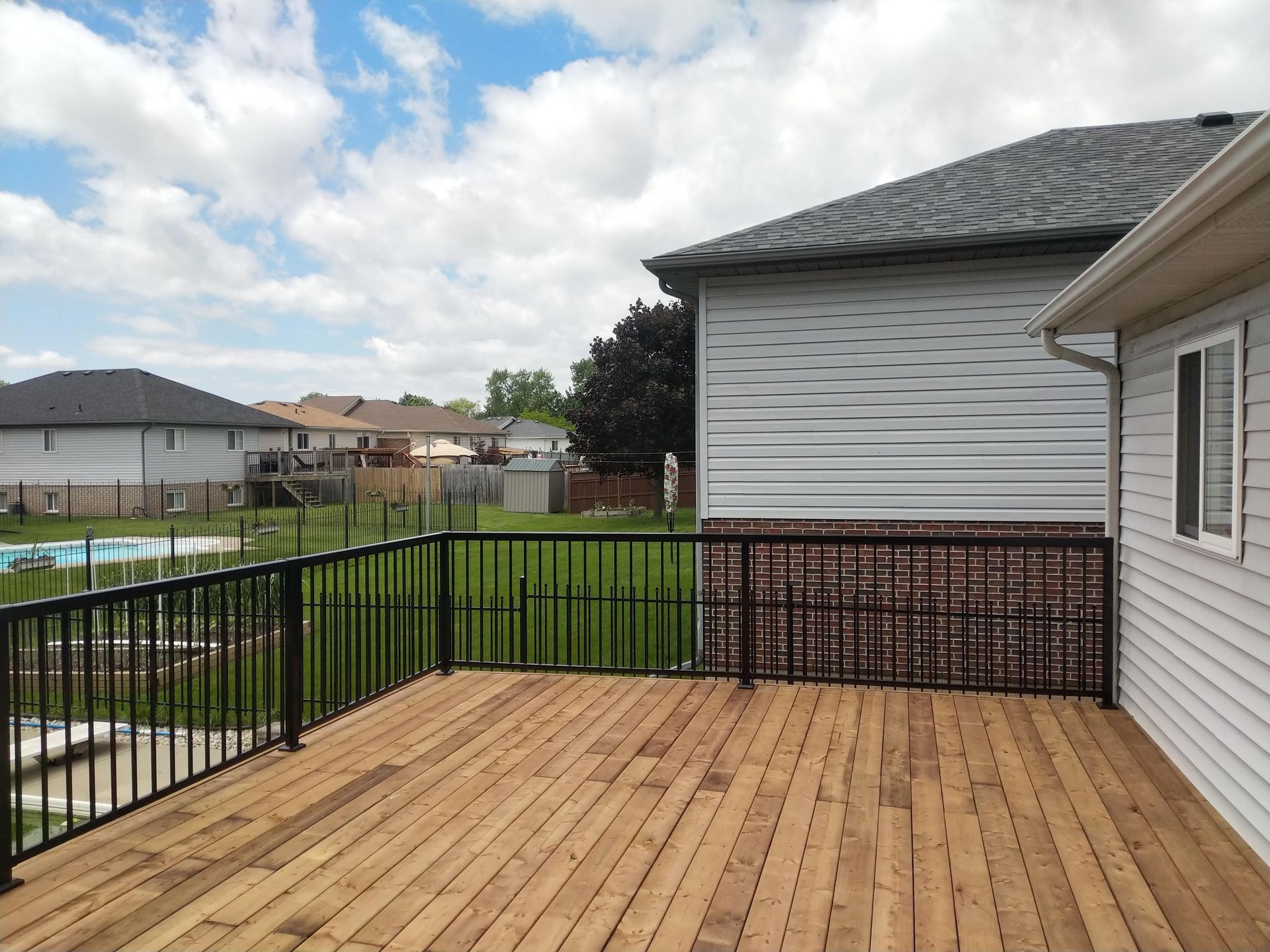 Wooden deck with black railings, attached to a house with white siding, overlooking a backyard.