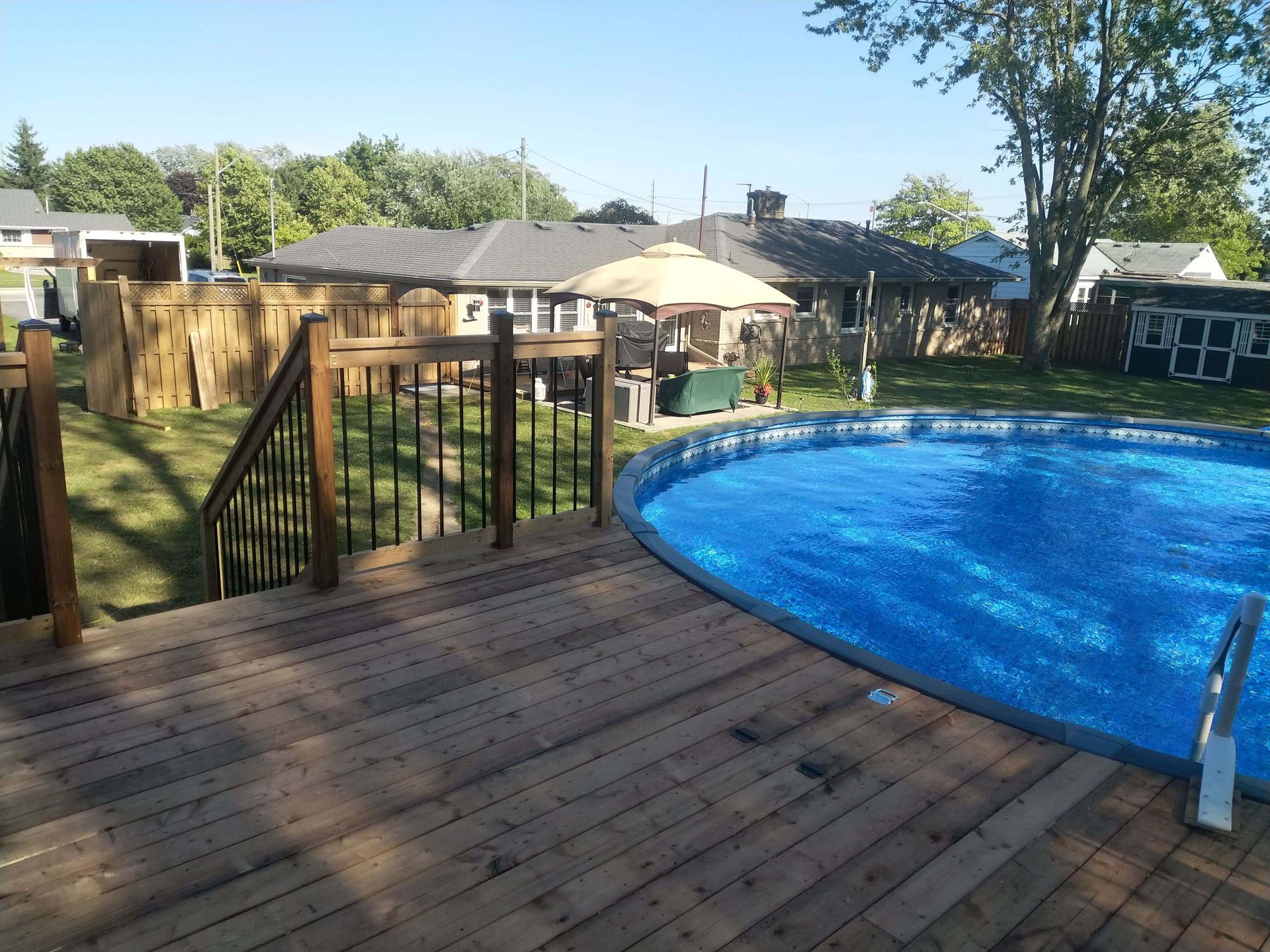 Wooden deck overlooking a backyard with an above-ground pool, fence, and houses in the background.