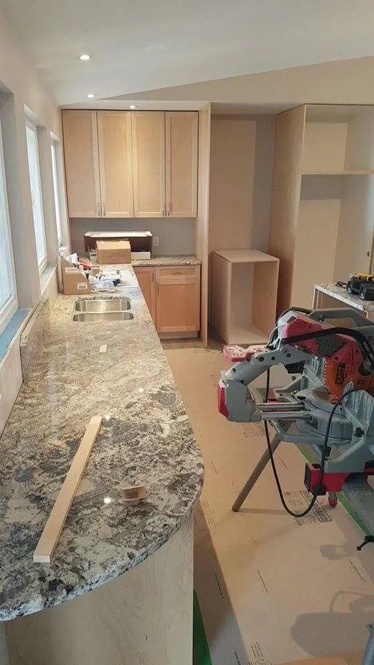 Kitchen under renovation: Granite countertop, light wood cabinets, sink, miter saw, and unfinished cabinet.