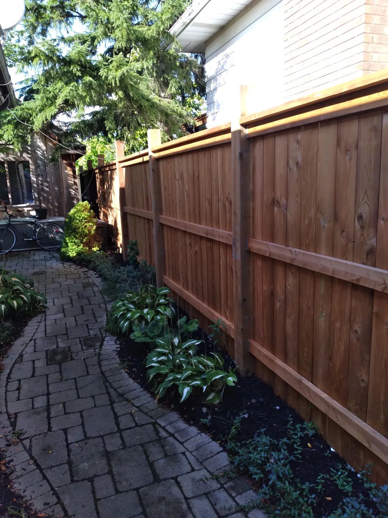 A wooden fence beside a brick pathway with a garden.