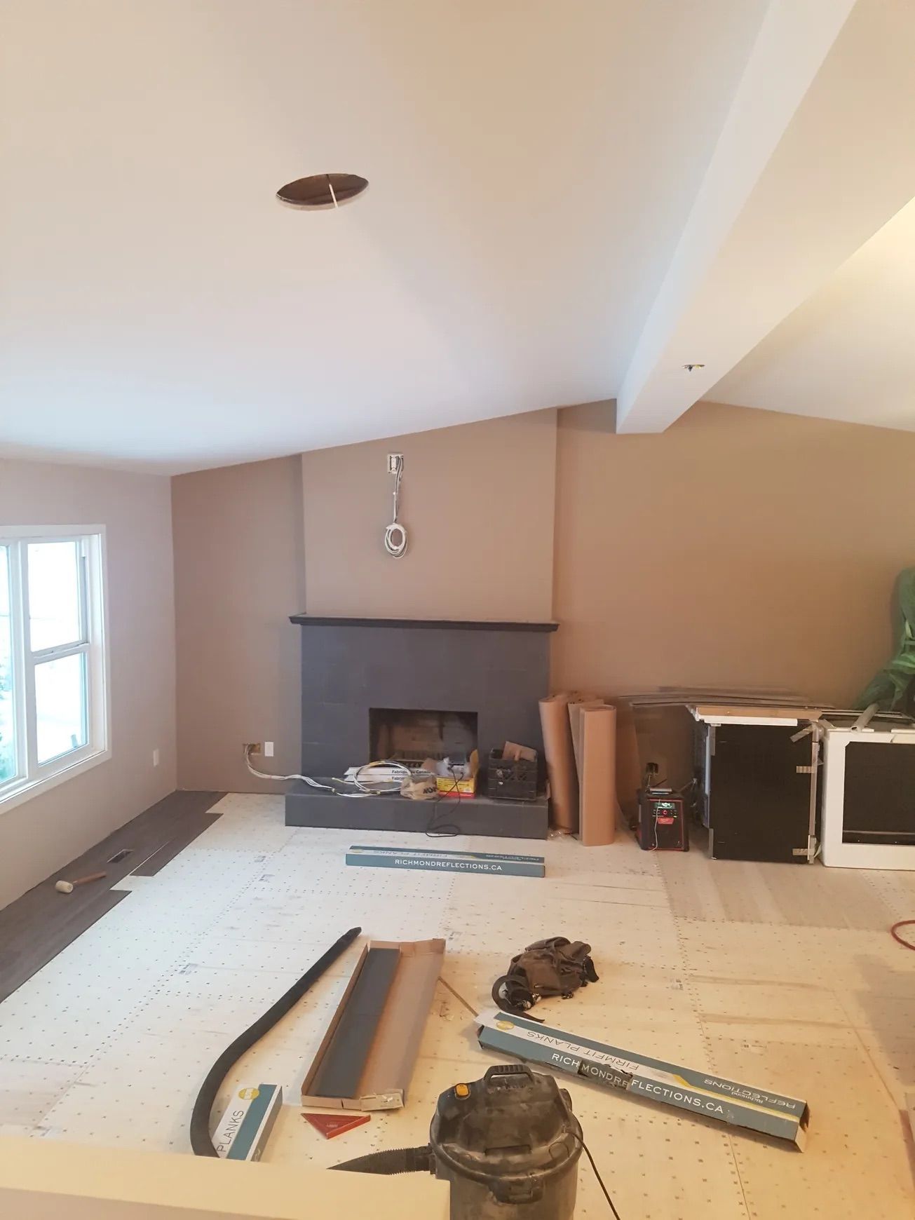 Living room under renovation with fireplace, tan walls, wood flooring, and tools.