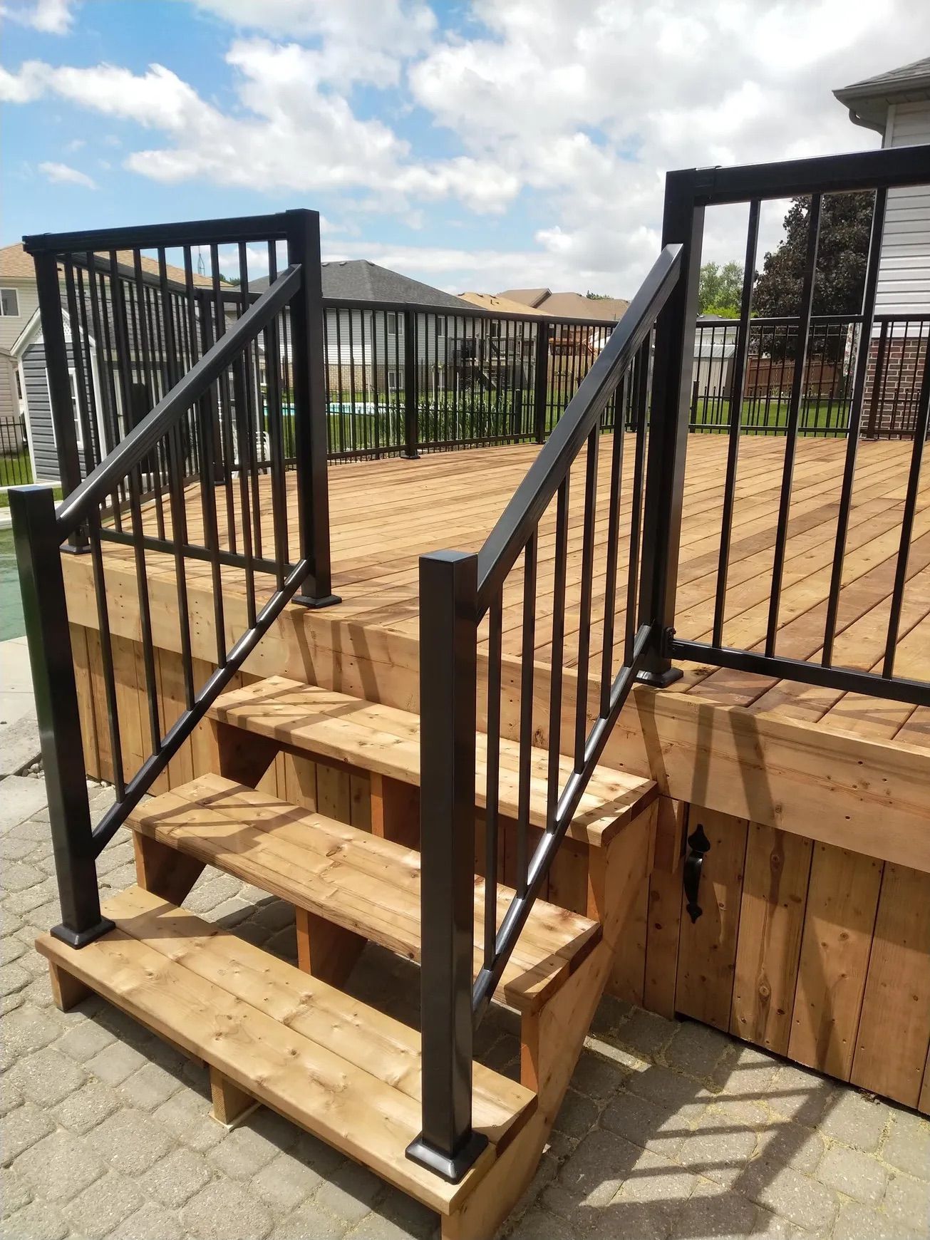 Wooden deck with black railings and steps leading down to a brick patio.