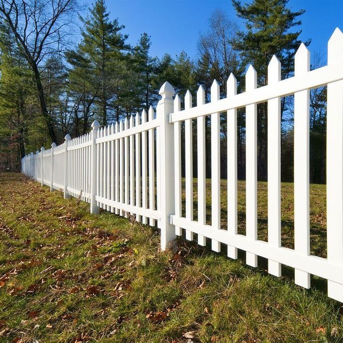 A white picket fence surrounds a grassy field with trees in the background