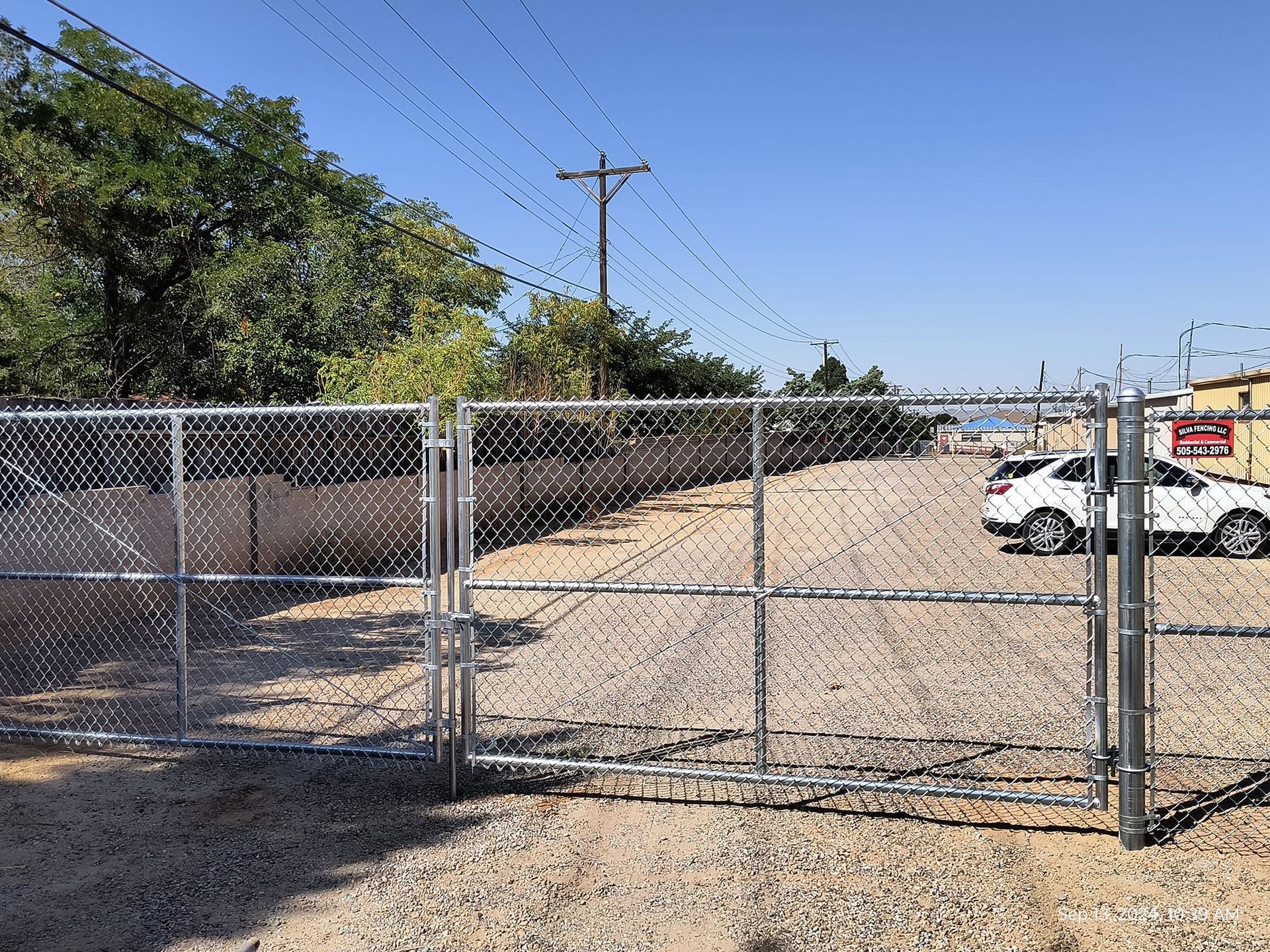 A chain link fence surrounds a gravel lot with a car parked in the background.