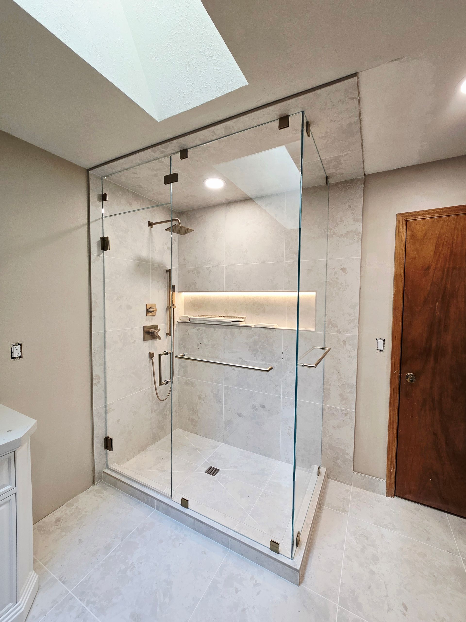 Modern bathroom with a glass shower enclosure, a skylight, and light gray tile.