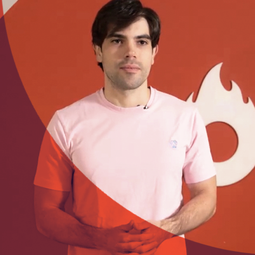 Um homem de camisa rosa está parado em frente a um fundo vermelho