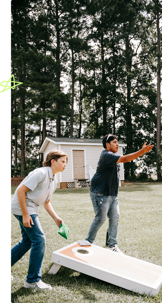 Two people outdoors playing cornhole, one tossing a bean bag toward the board.