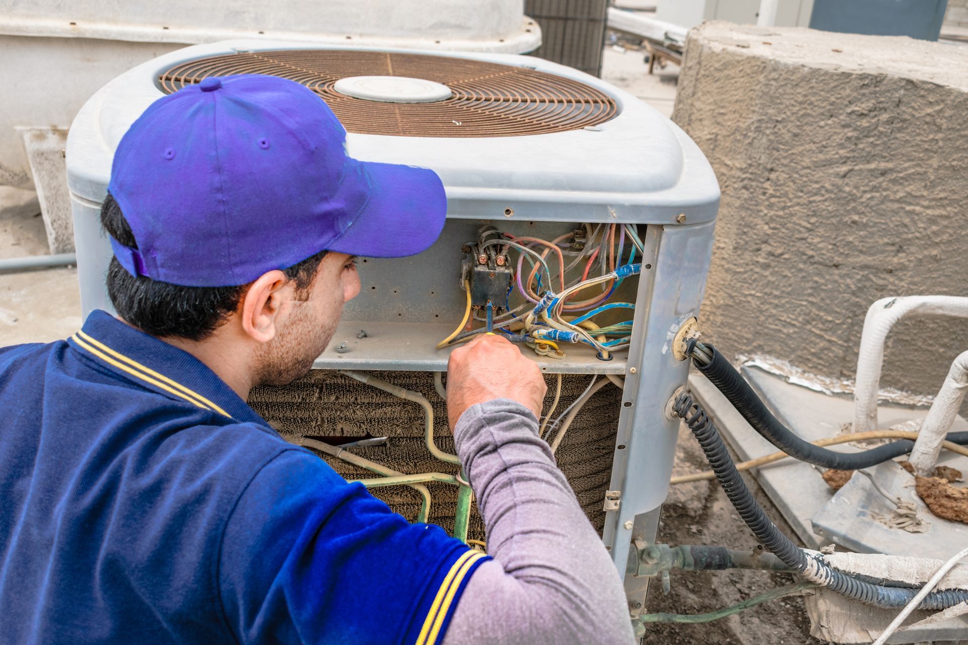 A Man in A Blue Hat Is Working on An Air Conditioner - Atlanta, GA - Dachi Mechanical