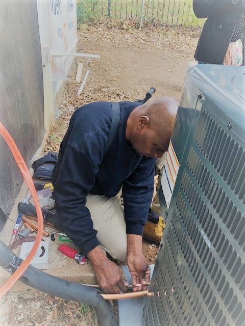 A Man Is Kneeling Down Working on An Air Conditioner - Atlanta, GA - Dachi Mechanical