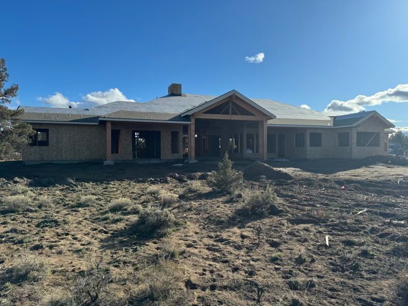 A large house is being built in the middle of a dirt field.