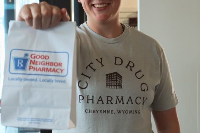 A woman wearing a city drug pharmacy shirt is holding a paper bag