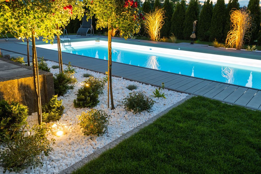 A large swimming pool is surrounded by trees and gravel in a backyard.