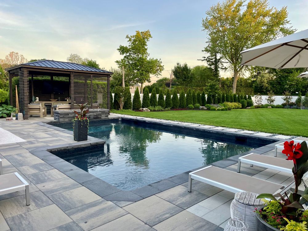 A large swimming pool is surrounded by chairs and umbrellas in a backyard.