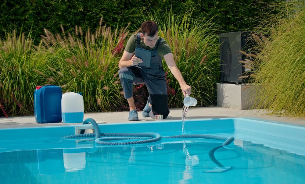 A man is kneeling next to a swimming pool.
