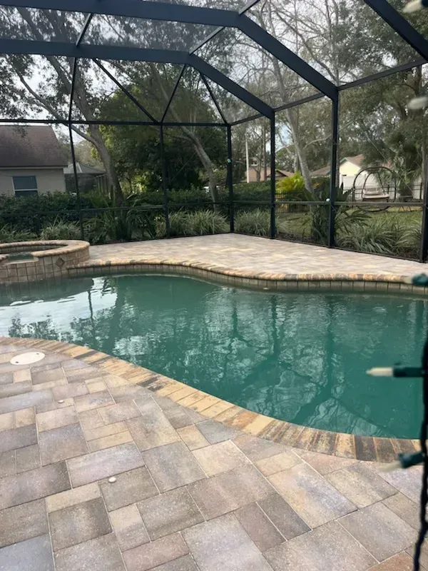 A large swimming pool is surrounded by a screened in area.