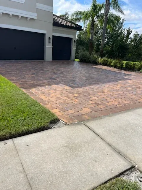 A brick driveway in front of a house with two garage doors