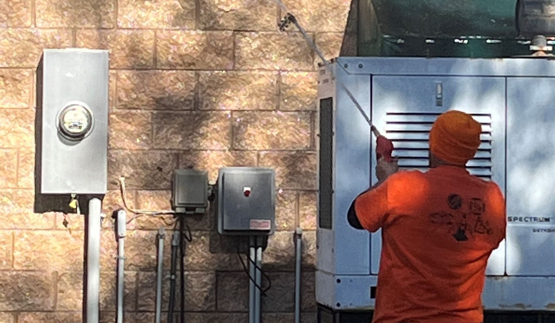 A man in an orange shirt is cleaning a brick wall with a hose.