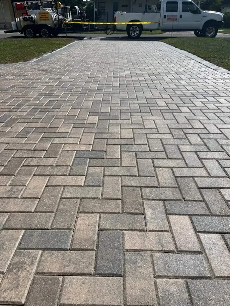 A white truck is parked on the side of a brick driveway.