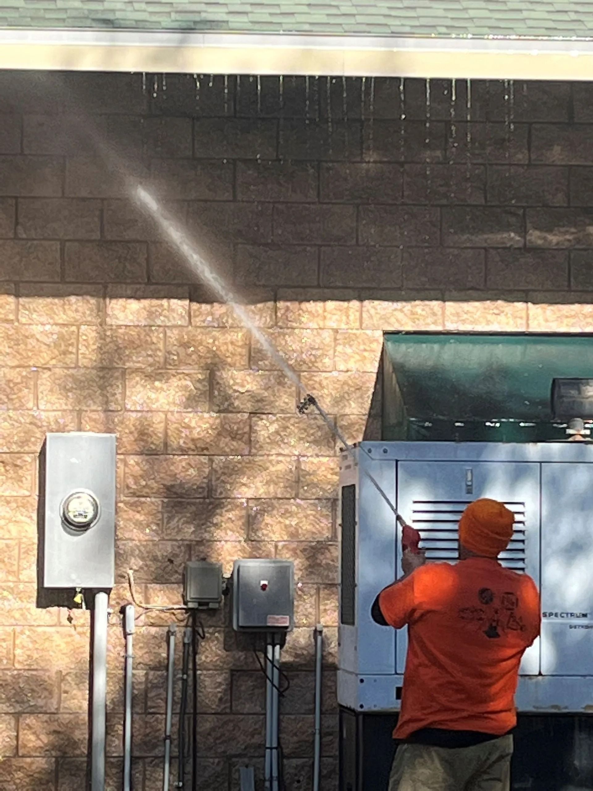 A man in an orange shirt is spraying water on a brick wall