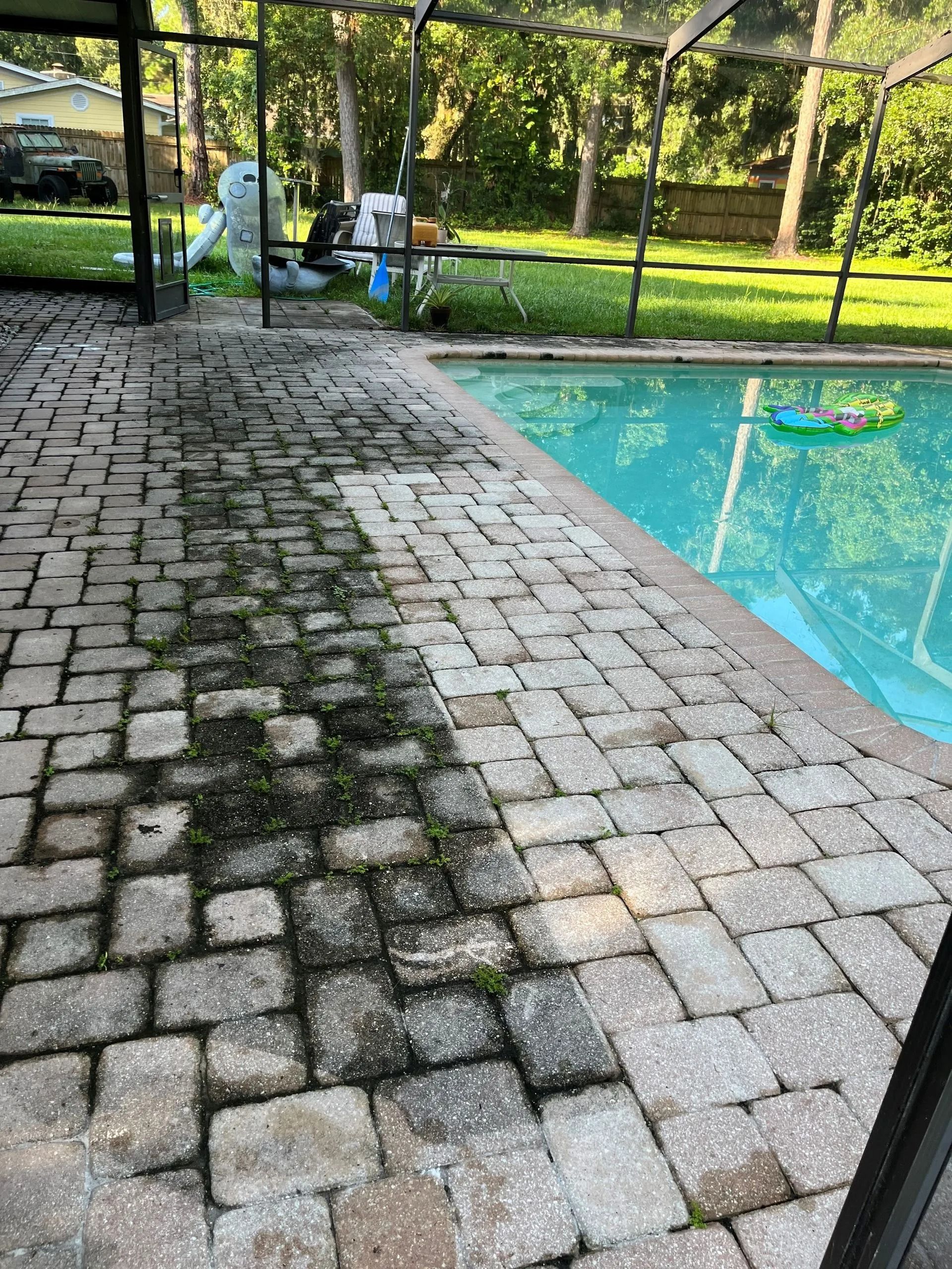 A brick patio next to a swimming pool with moss growing on it.