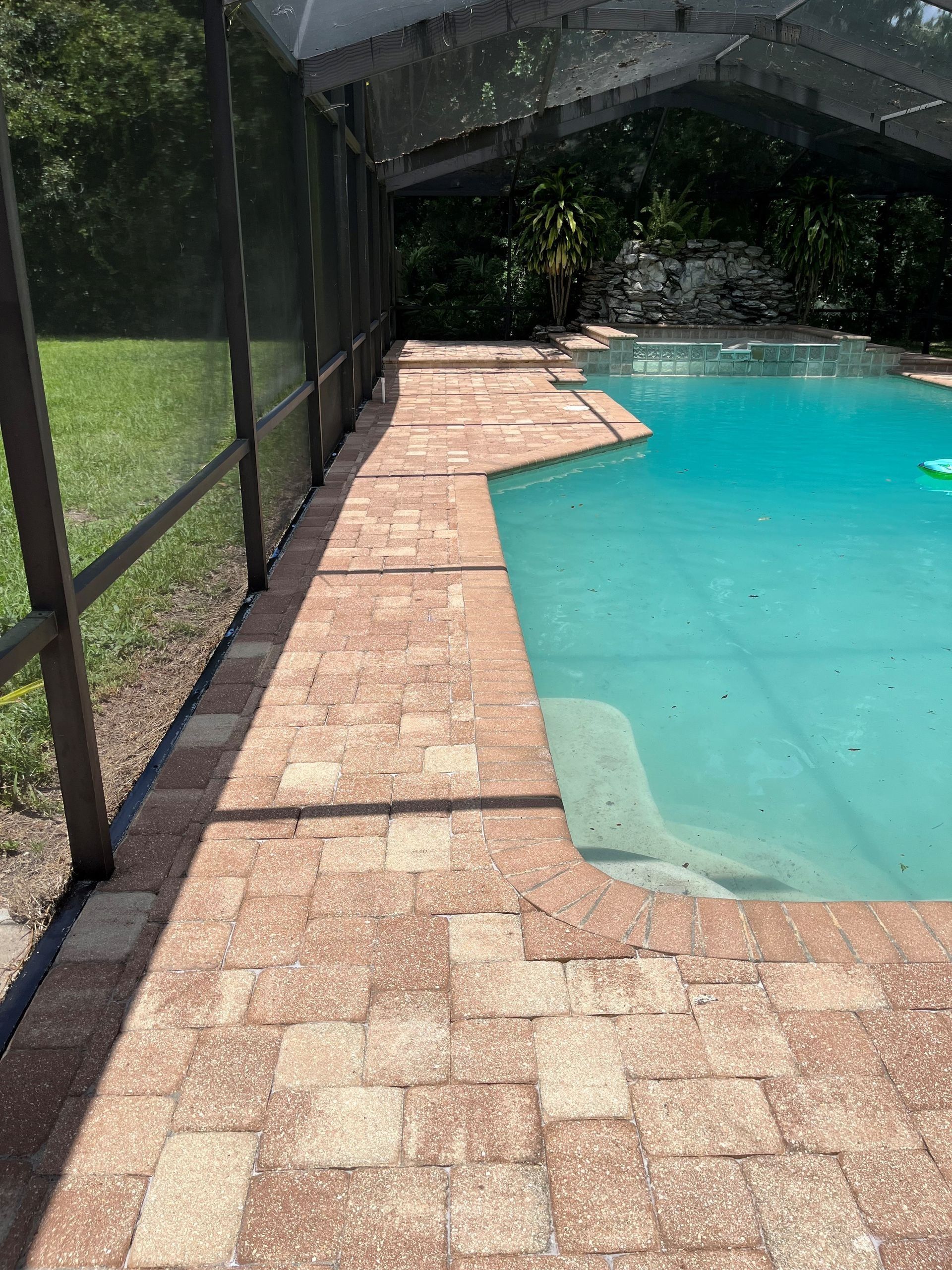 A swimming pool with a screened in area and a brick walkway leading to it.
