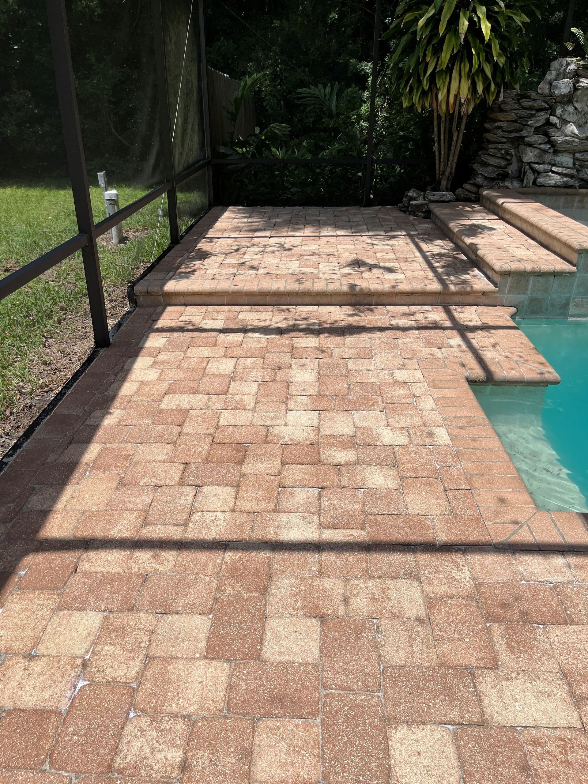 A brick patio next to a swimming pool with a screened in area.