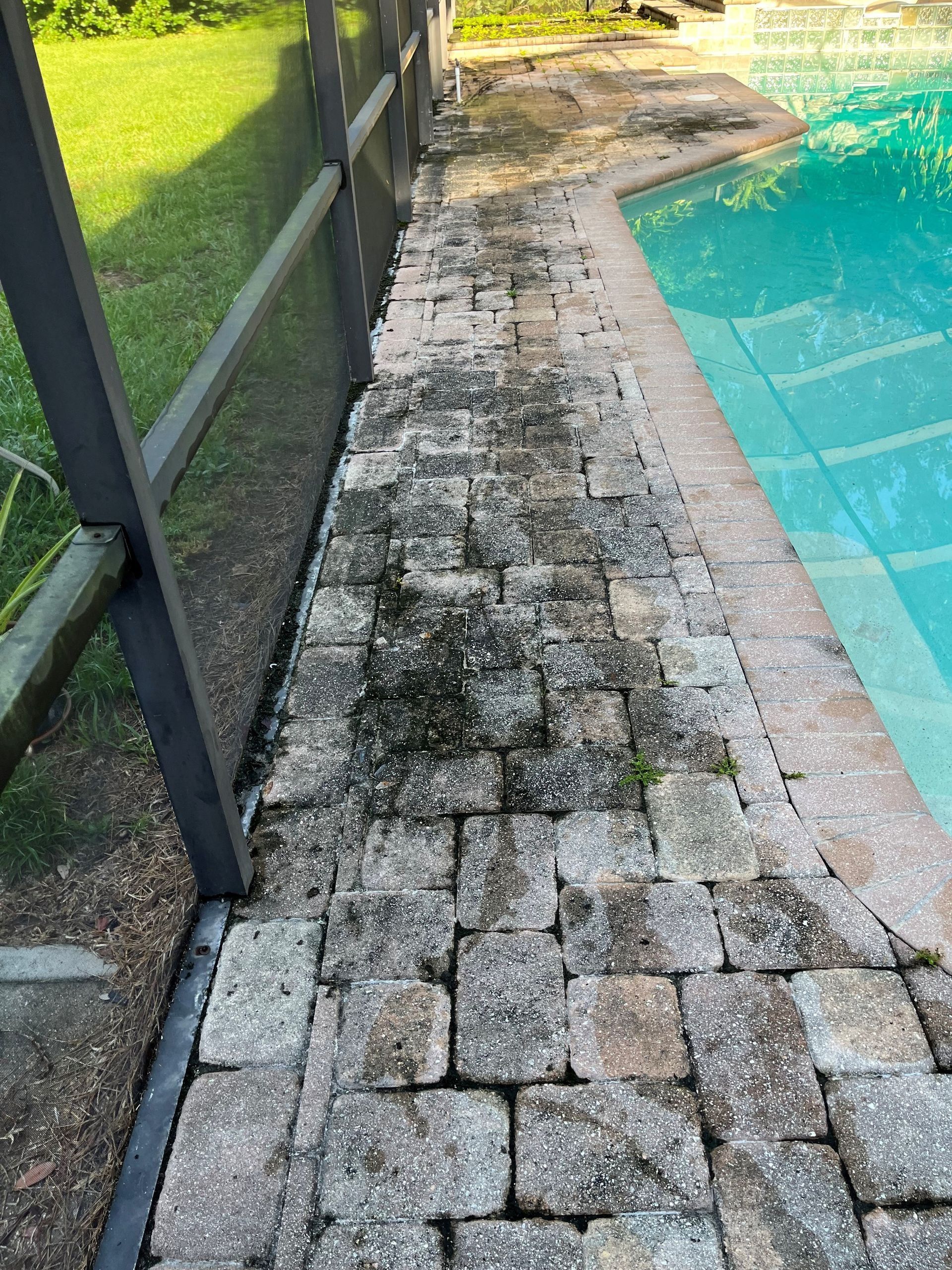 A dirty brick walkway next to a swimming pool.