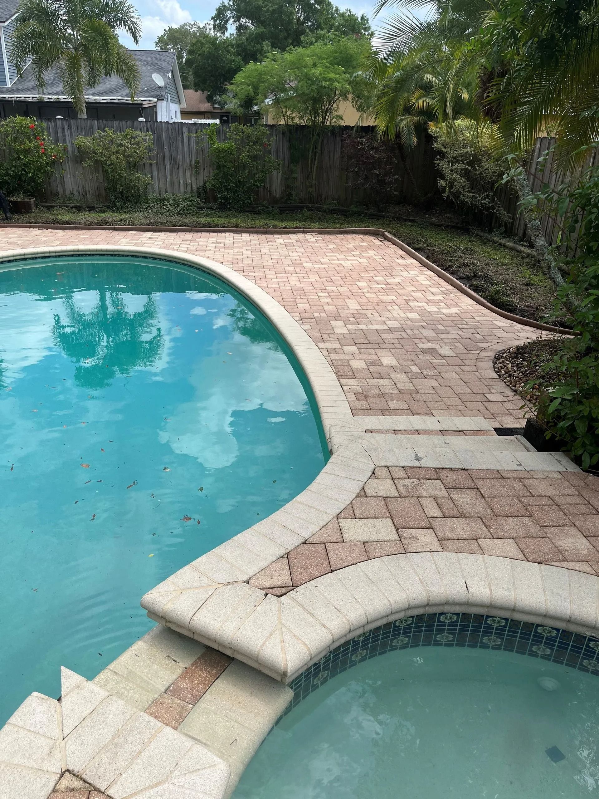 A large swimming pool with a brick walkway surrounding it.