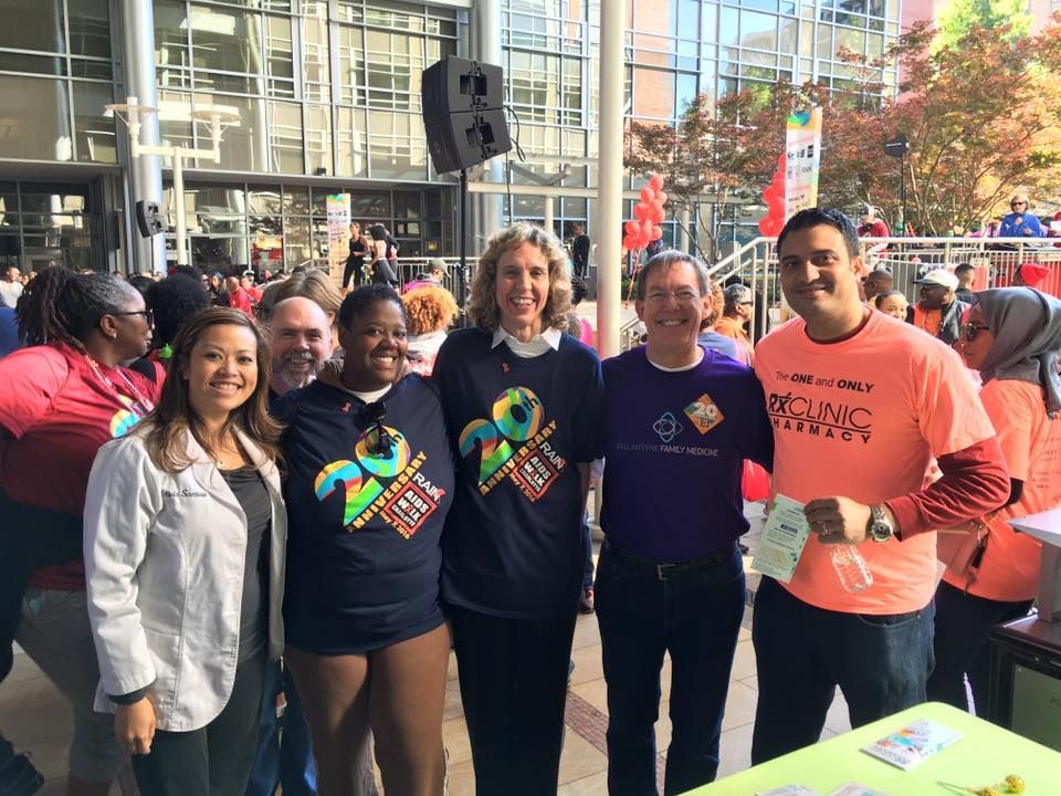Group of people smiling at an outdoor event, wearing shirts, standing near a building.