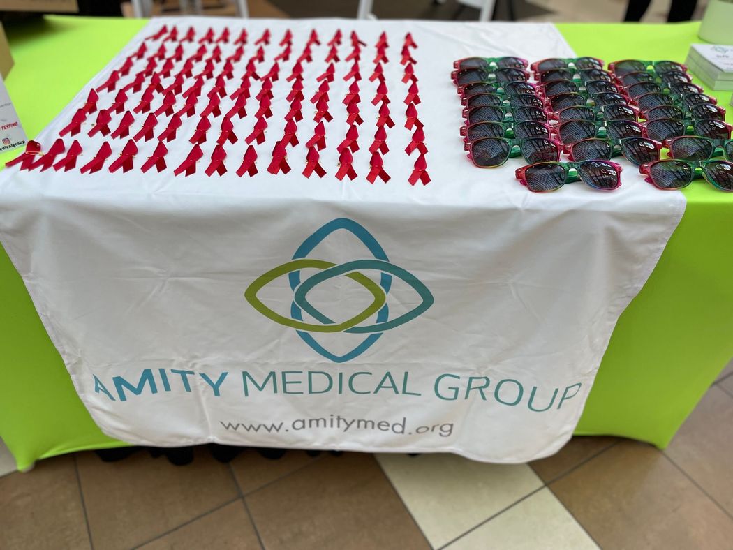 Table with Amity Medical Group logo, displaying red ribbon pins and sunglasses.