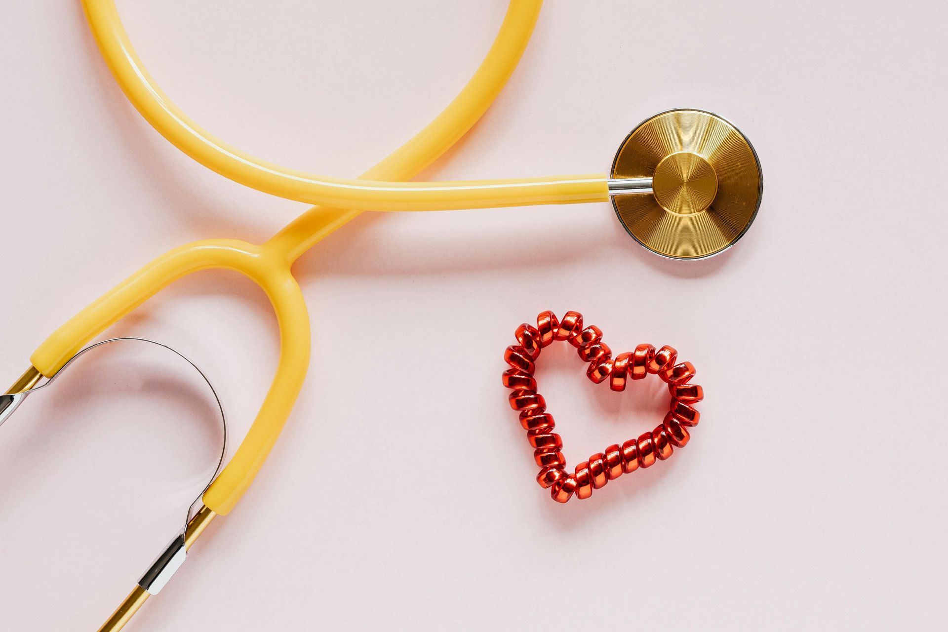 A stethoscope and a heart made of beads on a pink surface.