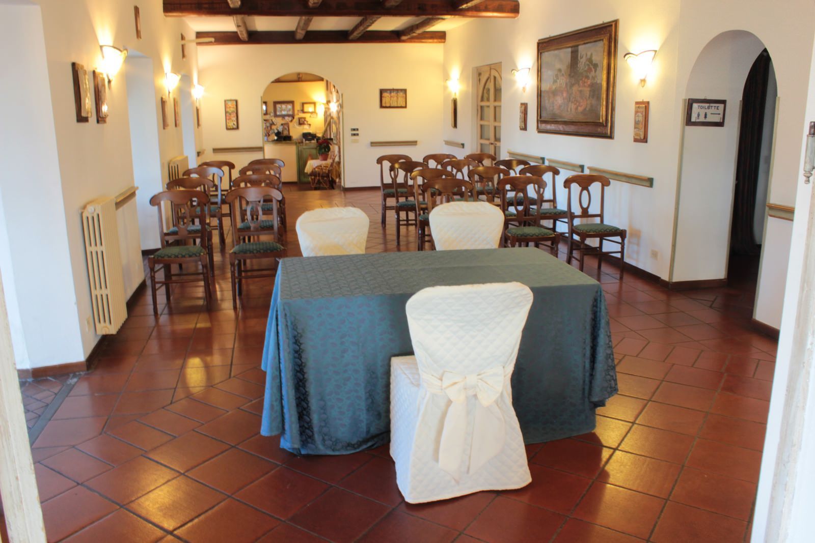 Una sala interna allestita per una cerimonia con sedie, tavolo e decorazioni.