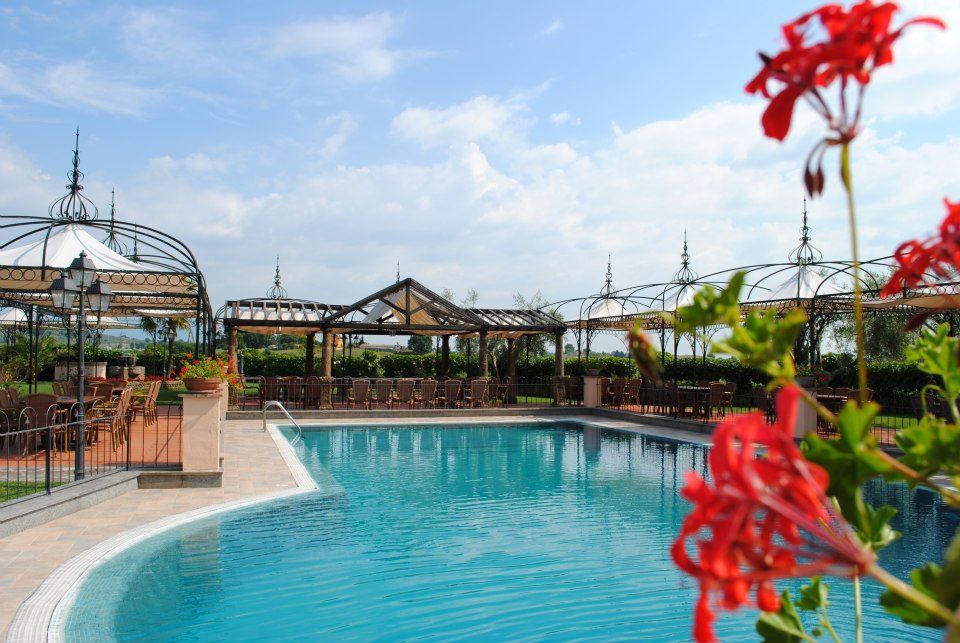 Piscina del resort, fiori rossi in primo piano, cielo azzurro, posti a sedere all'ombra.