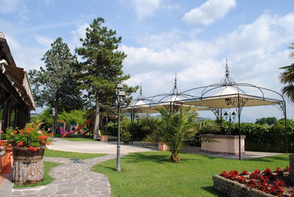 Lussureggiante area pranzo all'aperto con gazebo, fiori rossi e un sentiero in pietra sotto un cielo azzurro.