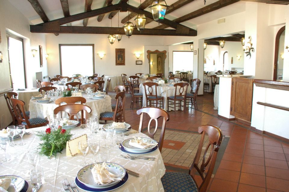 Sala da pranzo del ristorante con tavoli apparecchiati per gli ospiti, travi in ​​legno e pavimento piastrellato.