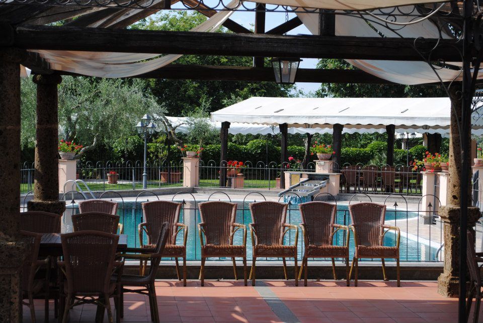 Ristorante a bordo piscina con tavoli e sedie sotto un pergolato, con vista sulla piscina e su un'altra zona pranzo.