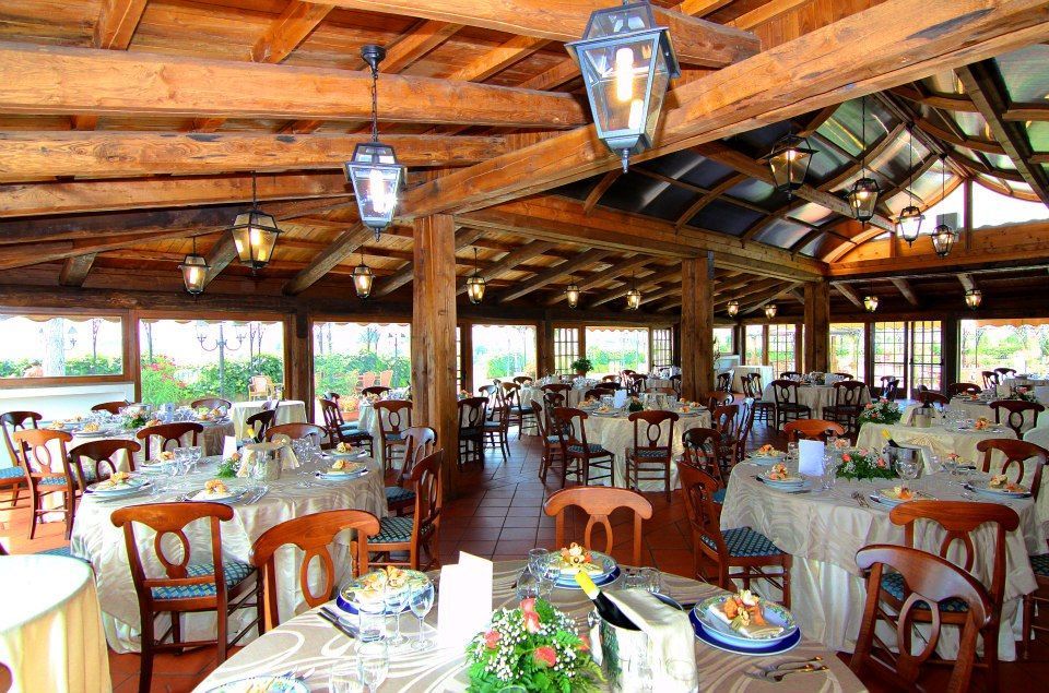 Interno del ristorante con tavoli rotondi apparecchiati per il pasto, travi in ​​legno, finestre e lanterne appese.