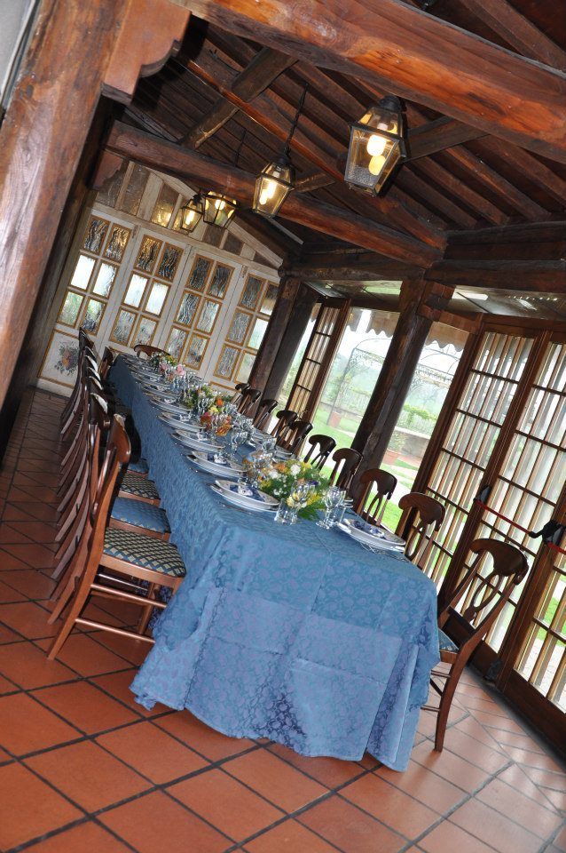 Lungo tavolo da pranzo apparecchiato per un pasto in una veranda con travi in ​​legno e ampie finestre.