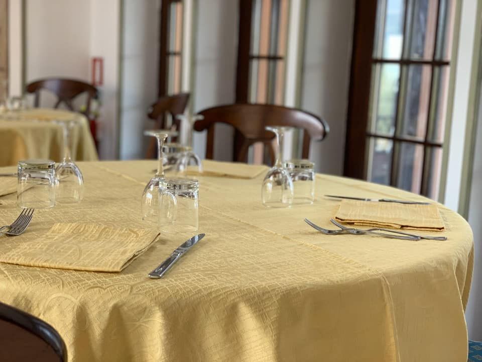 Tovaglia gialla su un tavolo rotondo apparecchiato per la cena, con bicchieri, posate e tovaglioli.