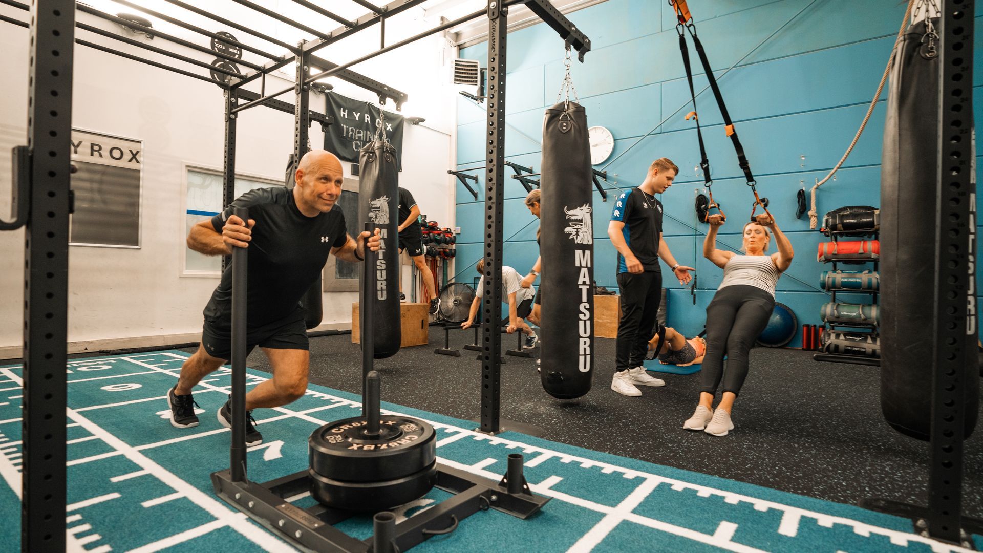 People training on suspension straps in a gym with blue walls and black equipment.